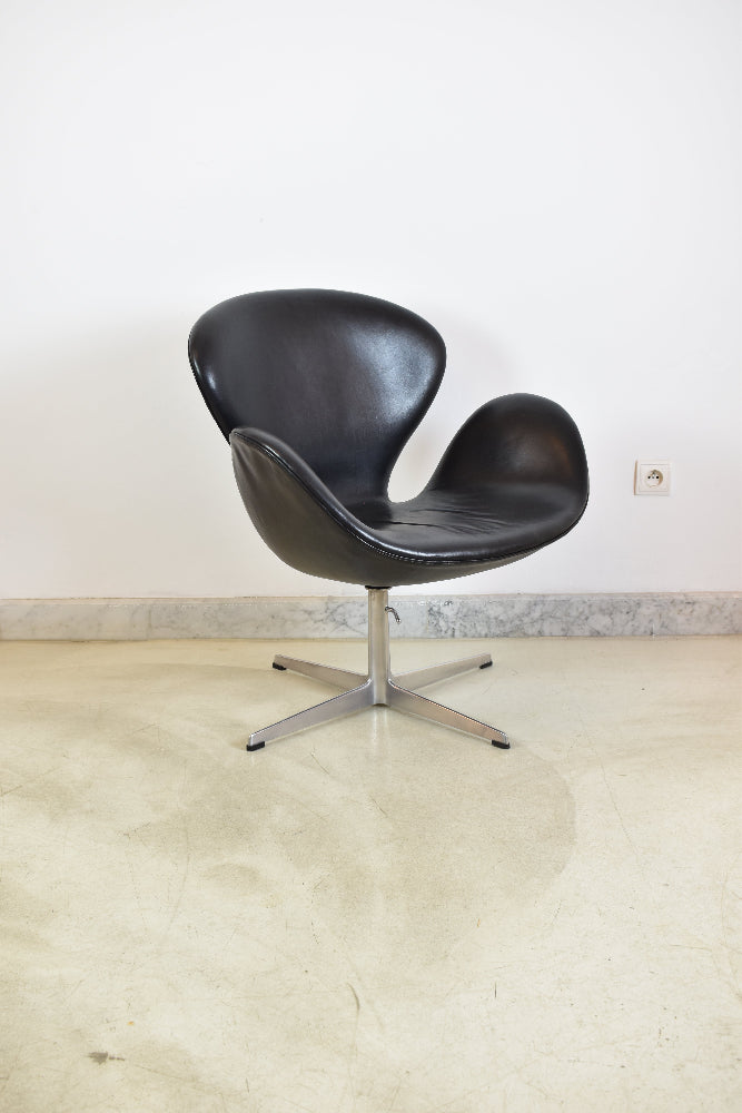 Angled front view of a sculptural black leather Swan lounge chair with an aluminum star pedestal base.
